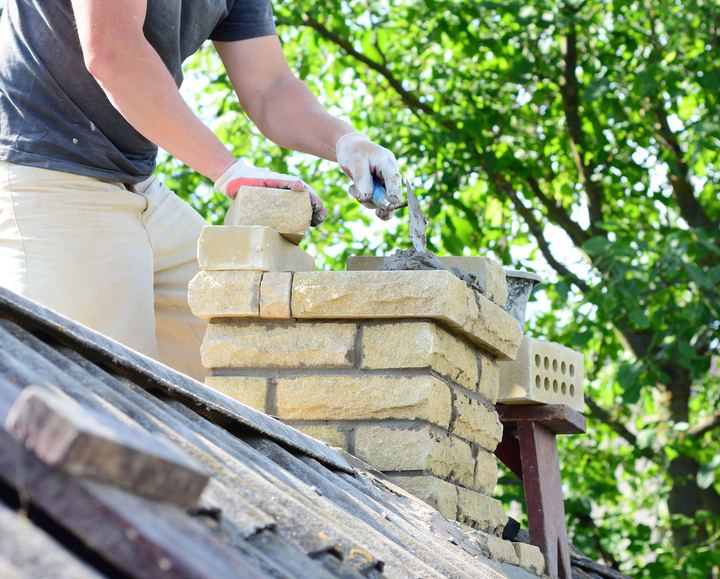 A mason laying buff brick on a chimney with a trowel and mortar.